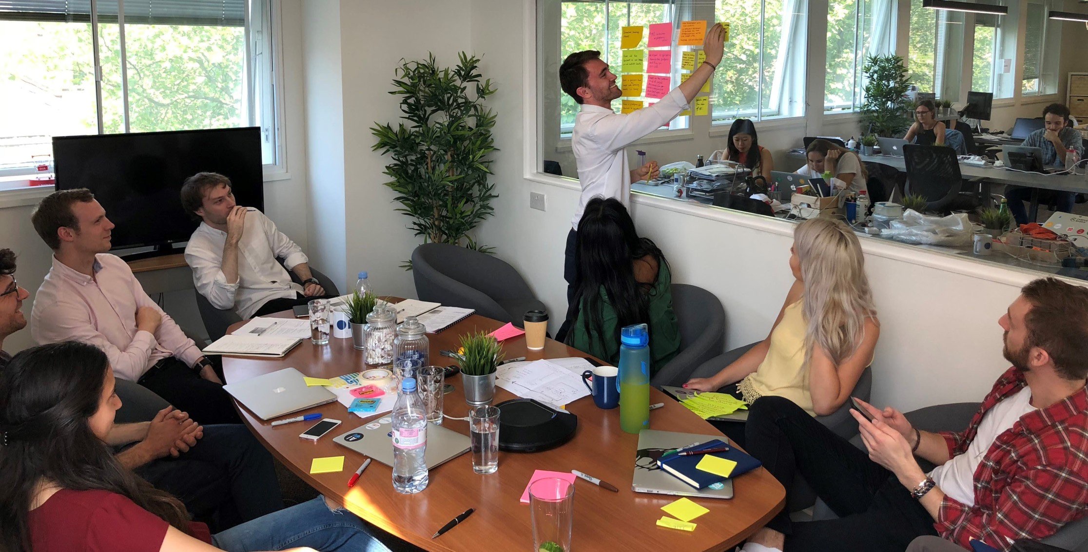 The mmtm team adding sticky notes to a window during a Discovery Workshop, with the group gathered around a meeting table
